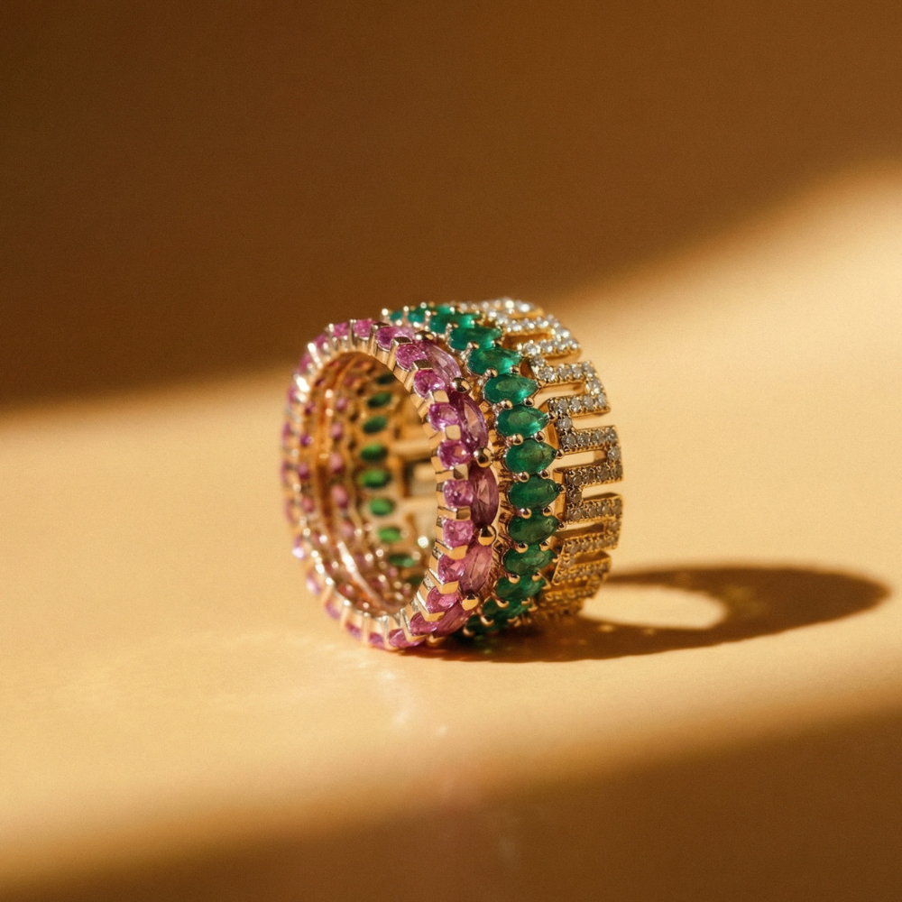 Stack of gold rings with green and pink gemstones on a beige background