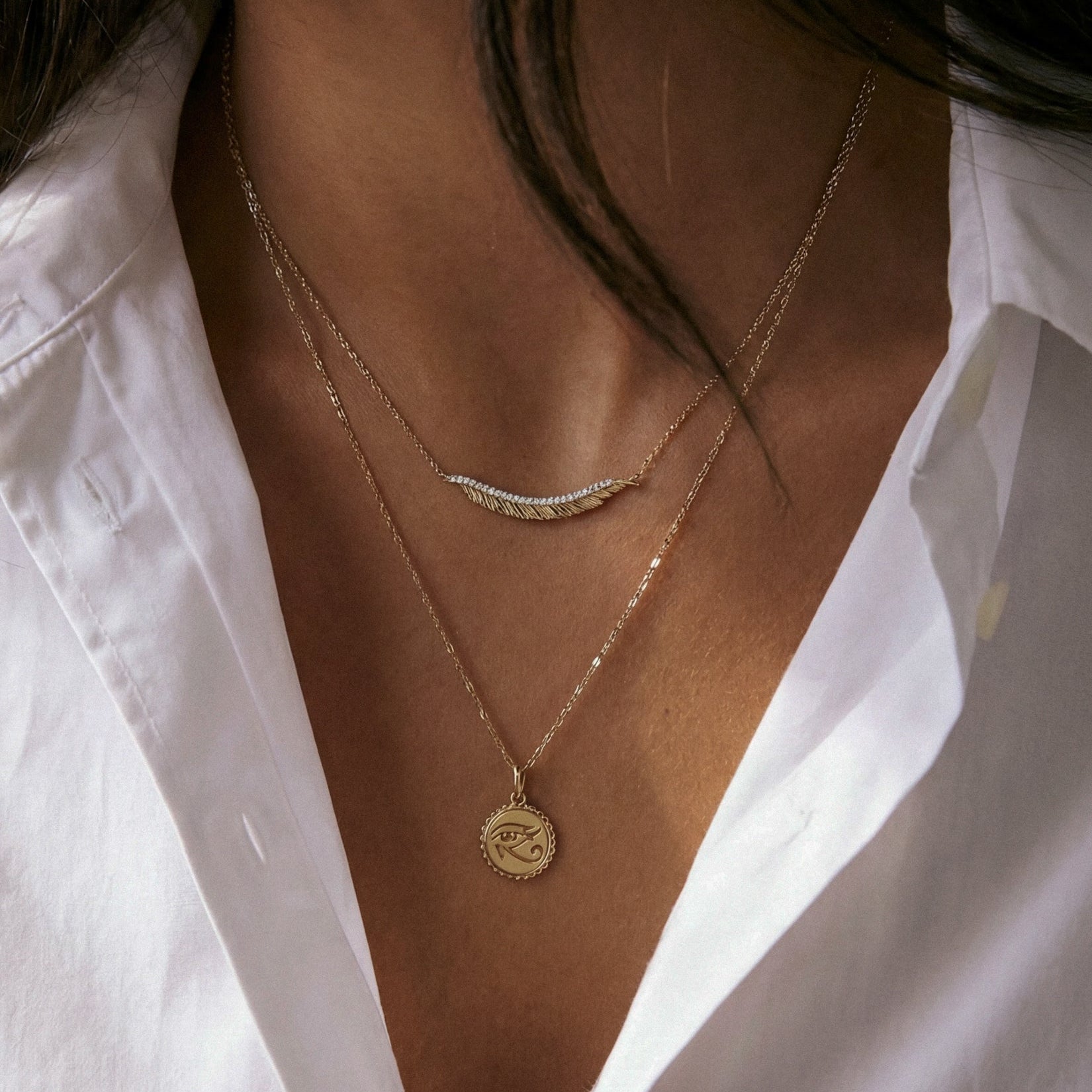 Close-up of a person wearing two gold necklaces against a white shirt.