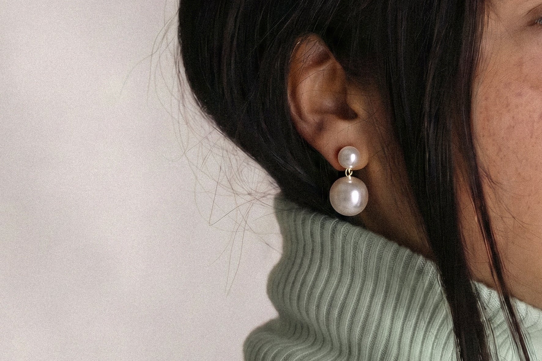 Close-up of a person wearing pearl earrings with a light background