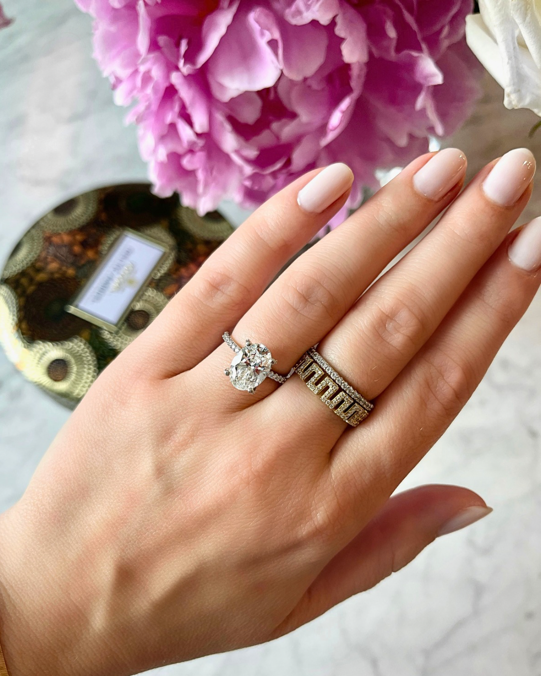 Hand wearing a diamond ring with a pink flower in the background