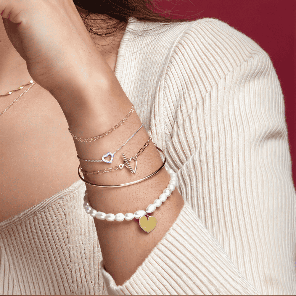 Close-up of a person's arm wearing multiple pearl bracelets with heart and triangle charms.