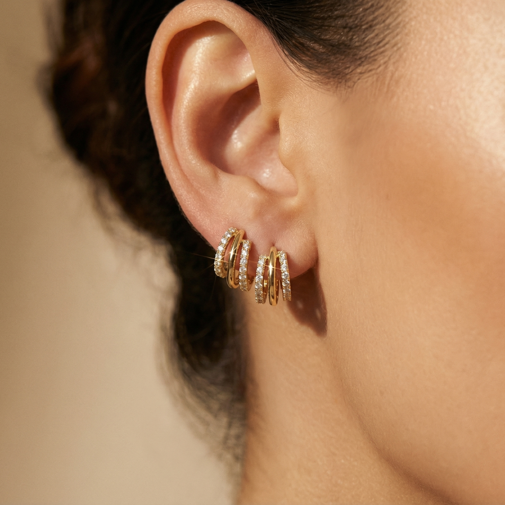Close-up of an ear wearing gold hoop earrings with a blurred background