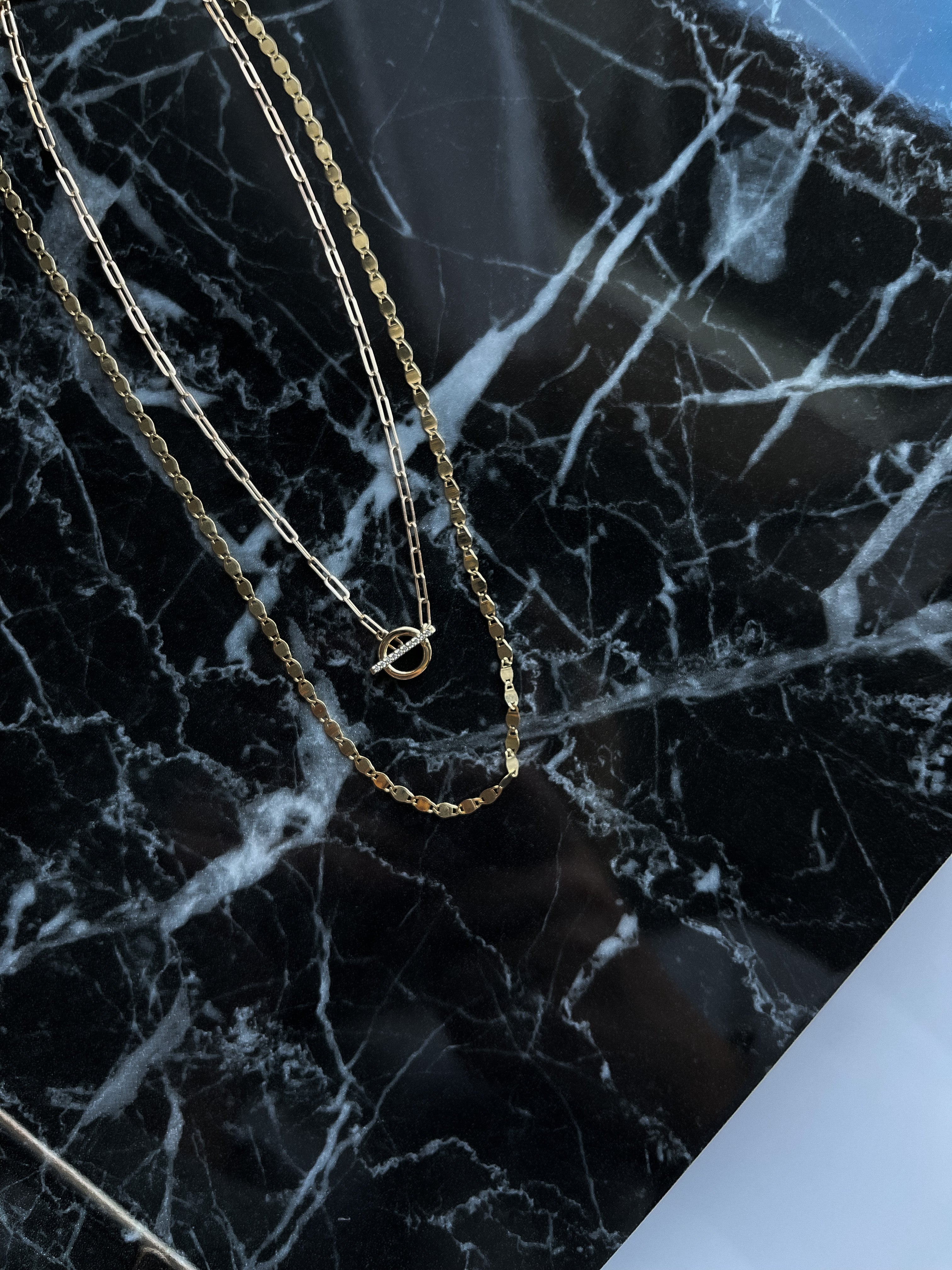 14k gold mirror link necklace  layered with another necklace on a black marble background