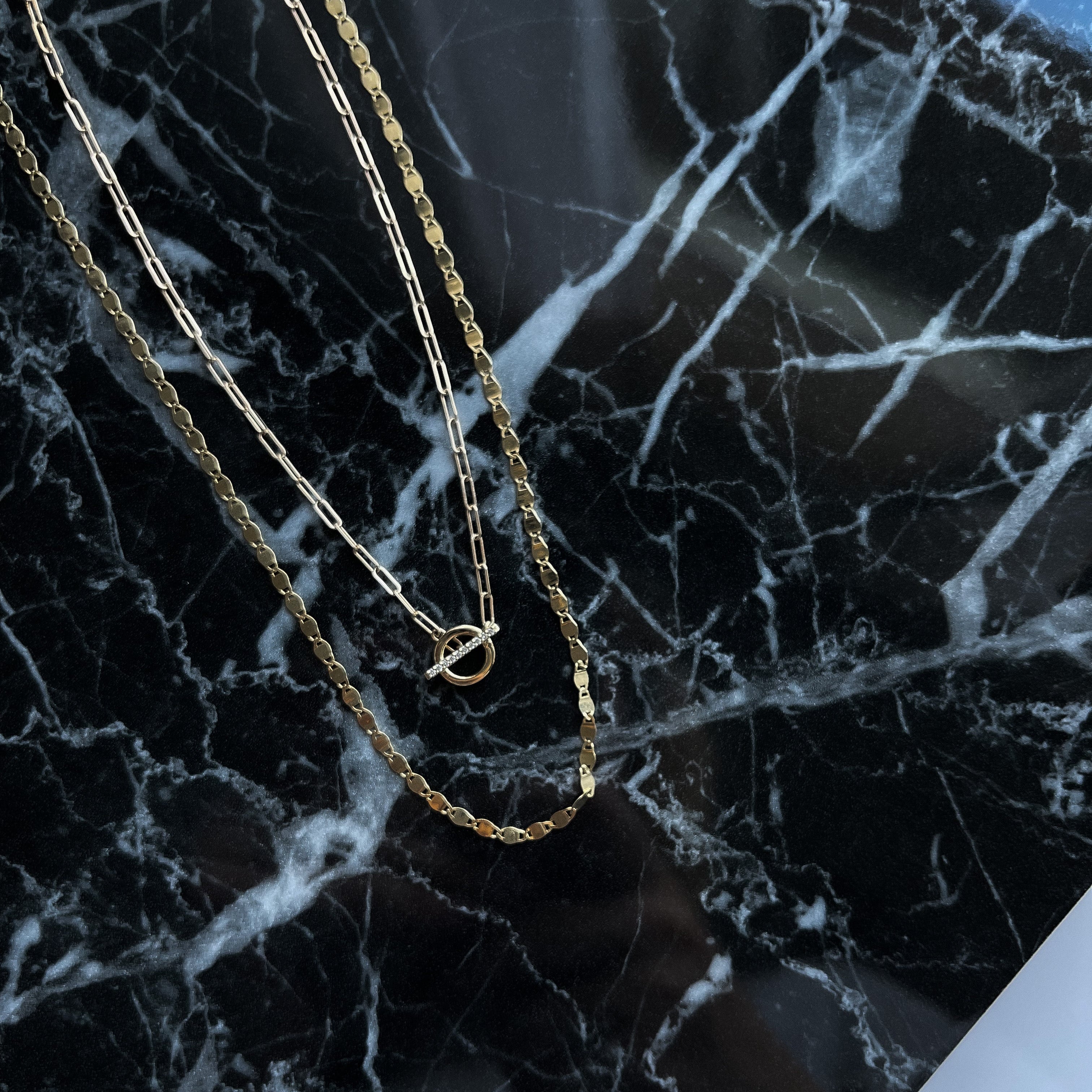 14k gold mirror link necklace layered with another necklace on a black marble background