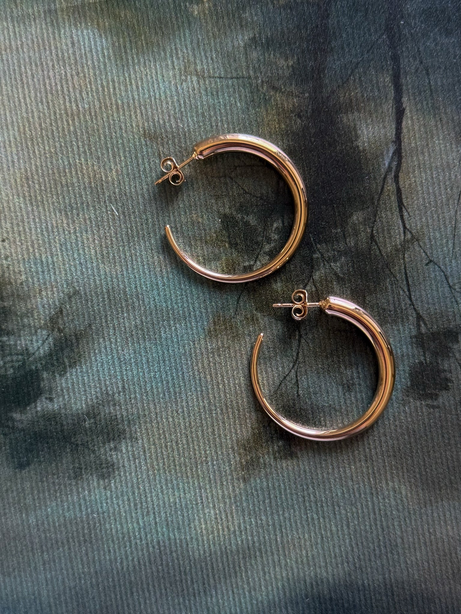 Gold hoop earrings on a textured green surface
