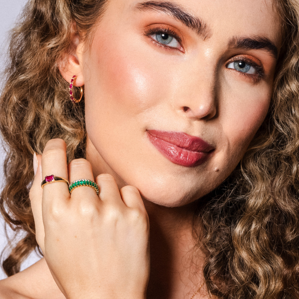 Close-up of a woman with curly hair wearing emerald jewelry on a neutral background
