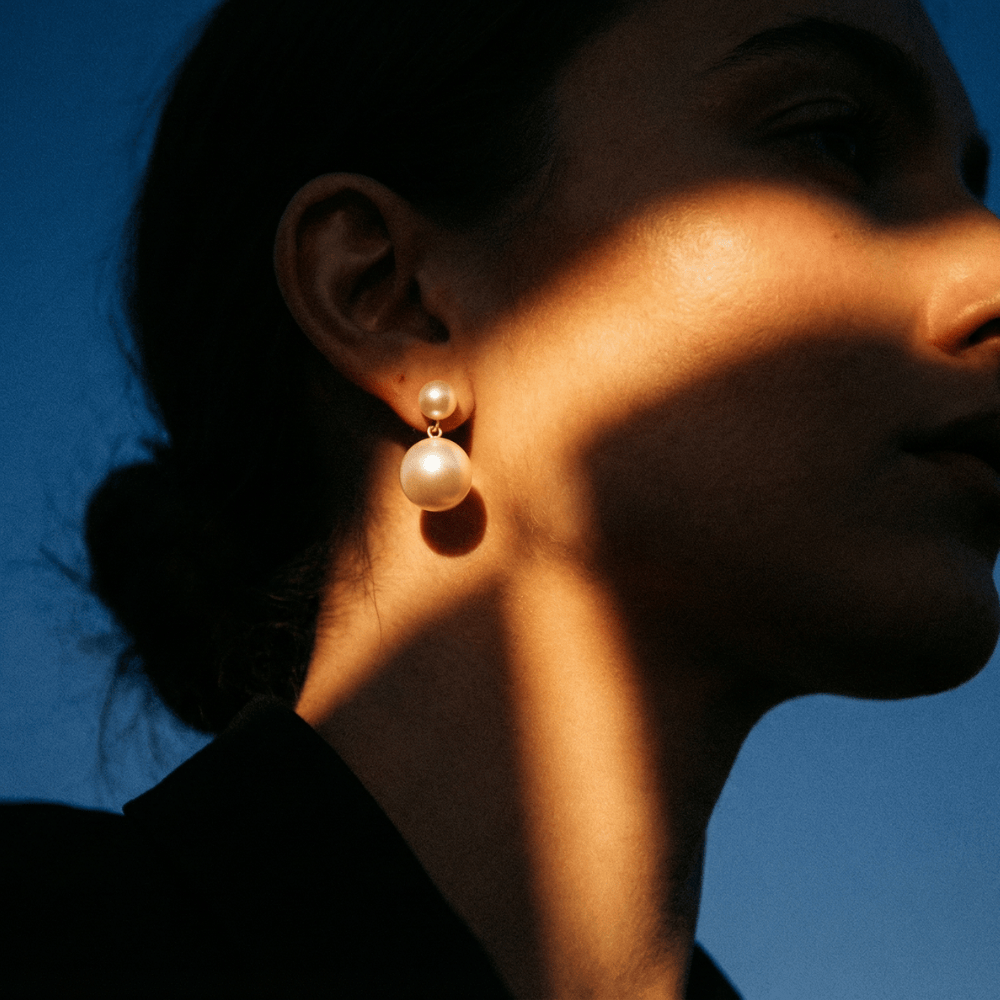 Close-up of a person wearing pearl earrings with a blue background
