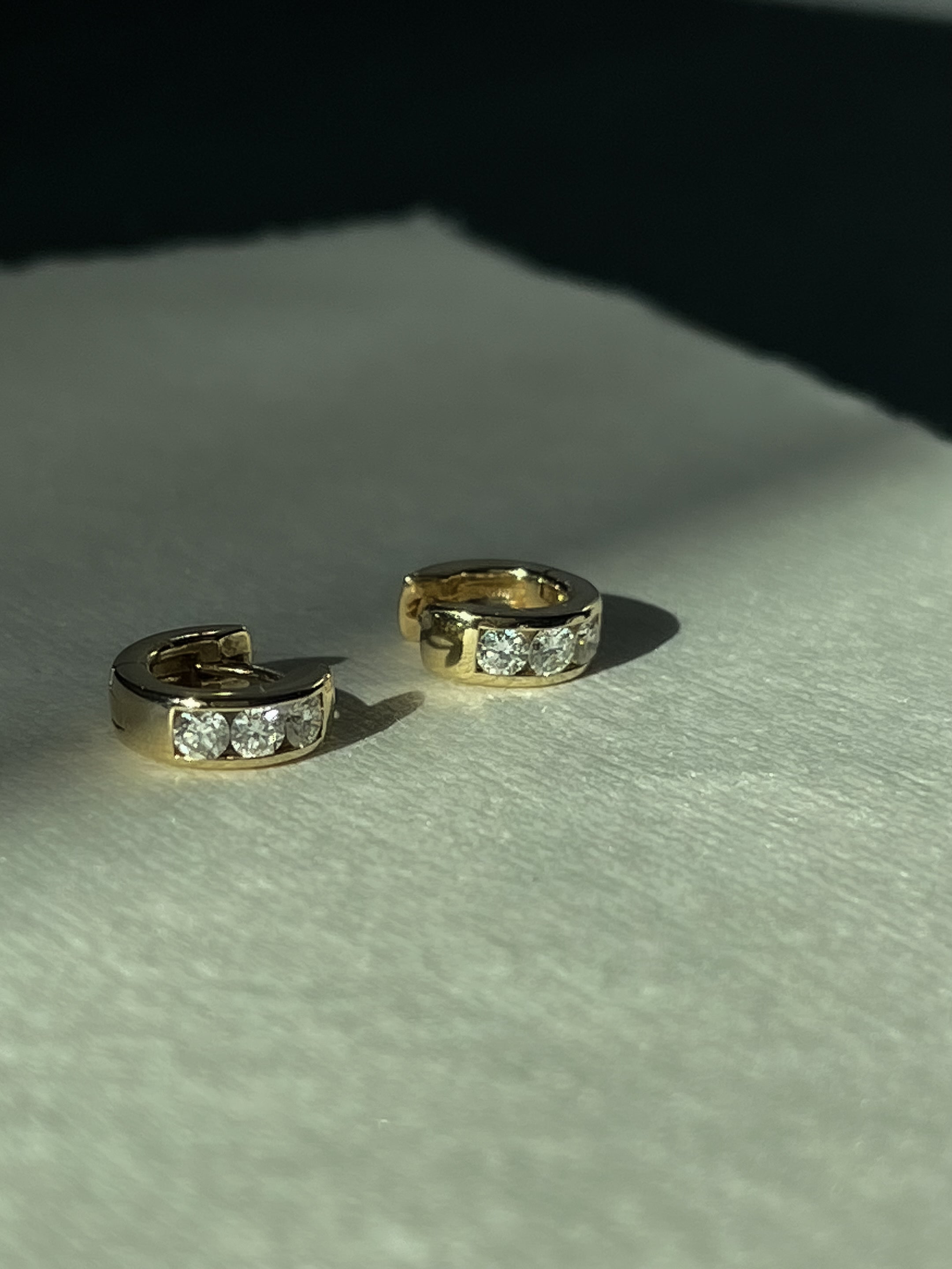 Gold hoop earrings with embedded diamonds on a textured surface