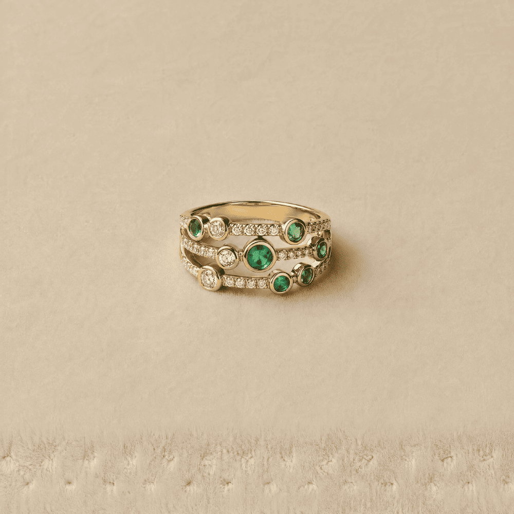 Gold ring with green gemstones on a beige background