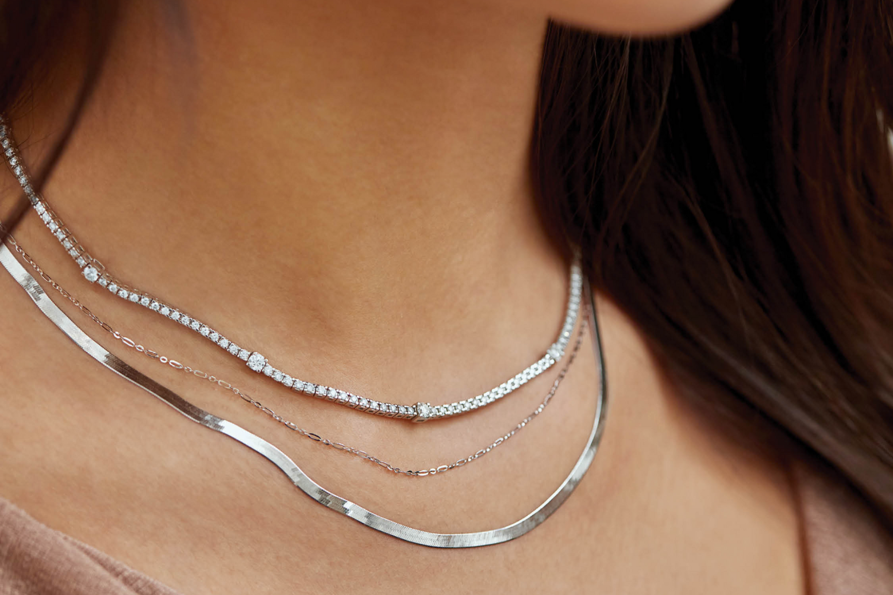 Close-up of a person wearing multiple silver necklaces on a blurred background