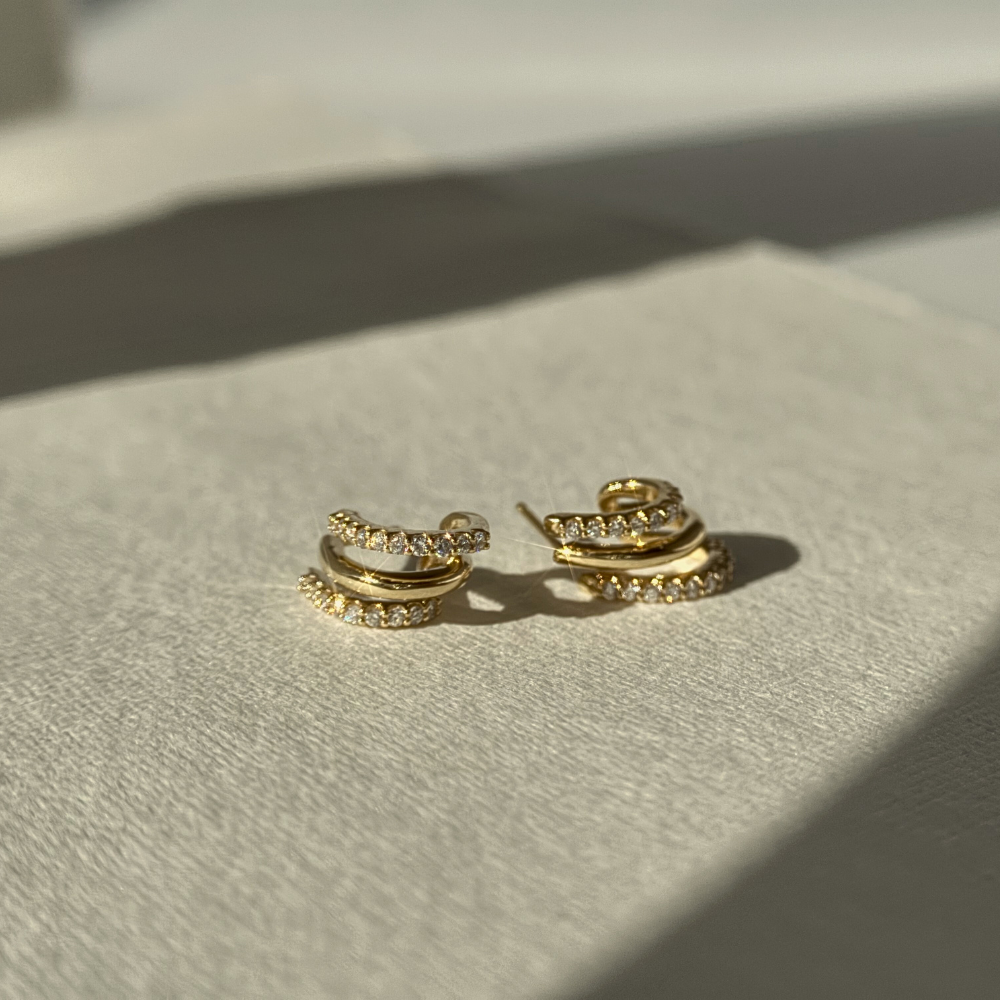 Gold hoop earrings on a light gray surface with soft shadows