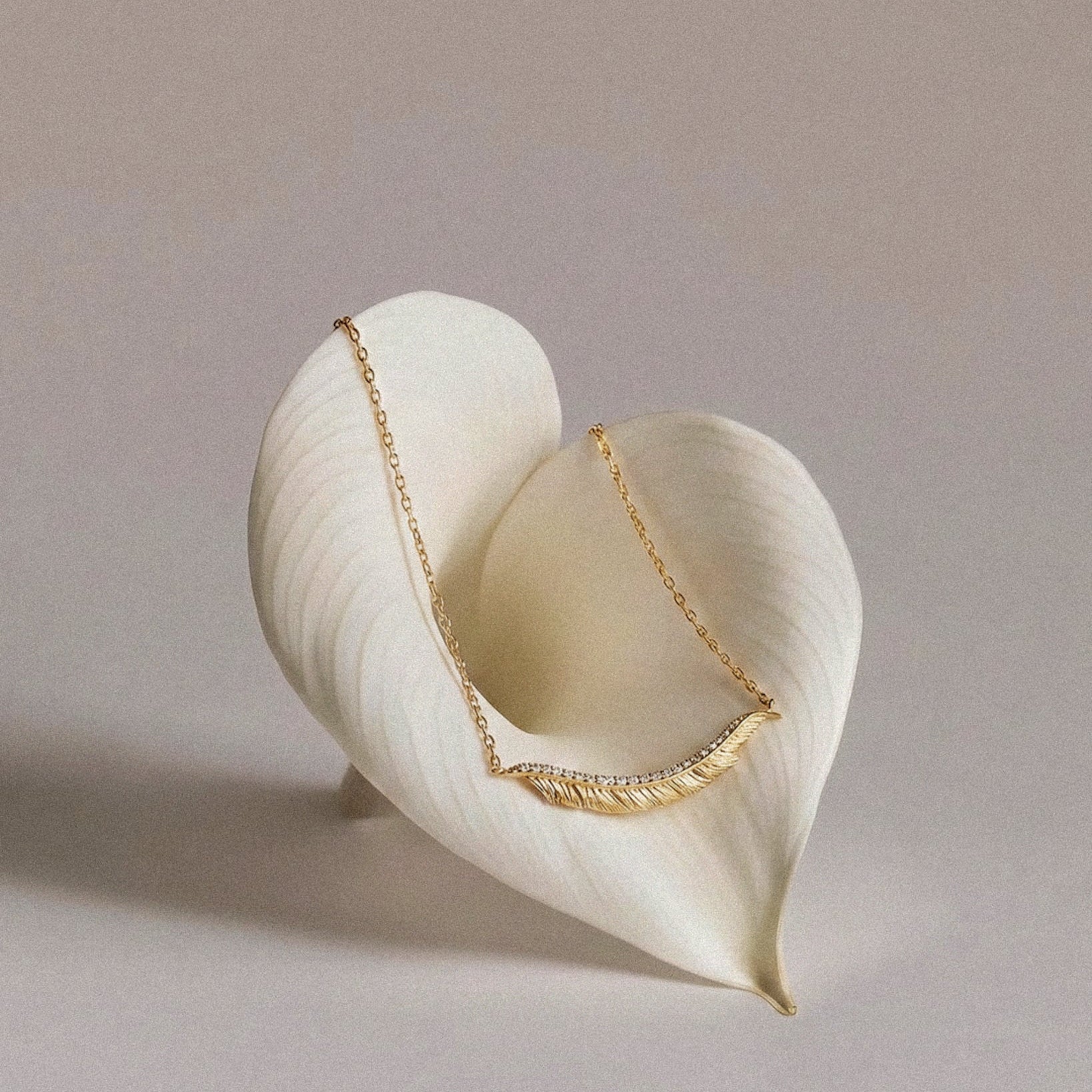 Gold feather necklace draped over a white shell on a neutral background