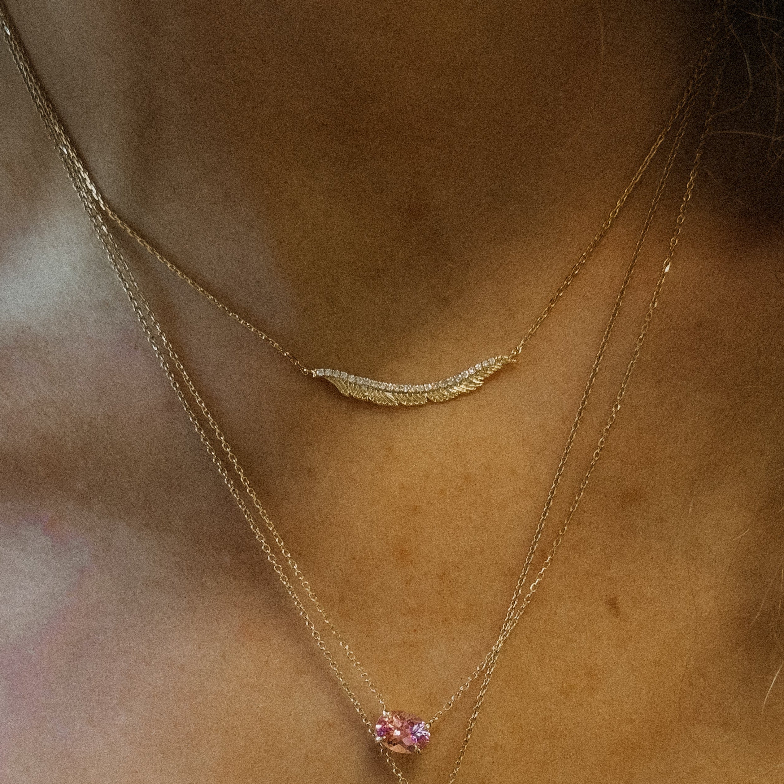 Close-up of a person wearing a gold feather necklace.