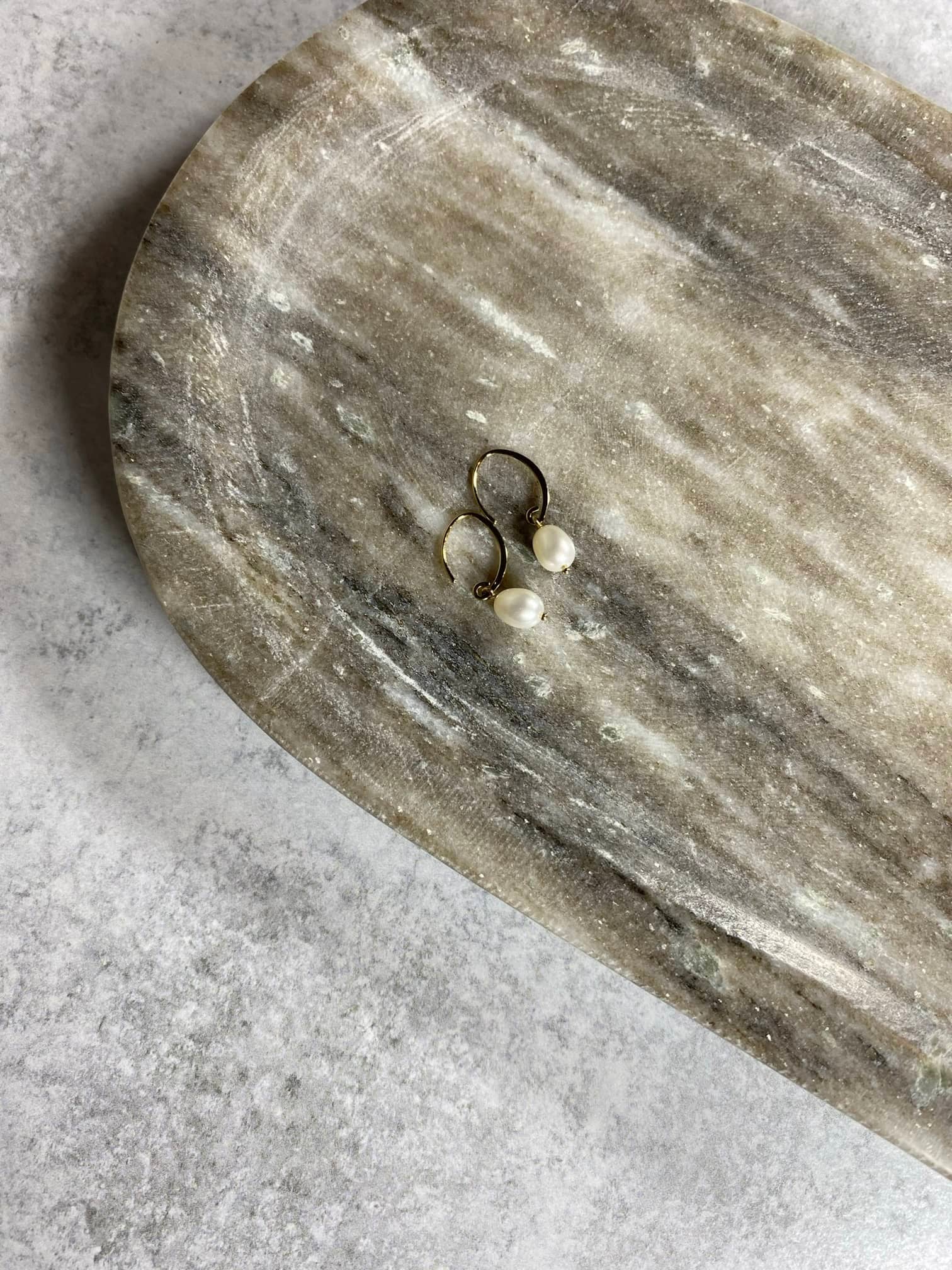 small 14k gold pearl earrings laying on a marble tray